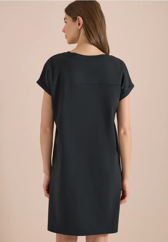 Rückenansicht einer Frau in schlichtem, knielangem schwarzen Kurzarmkleid.