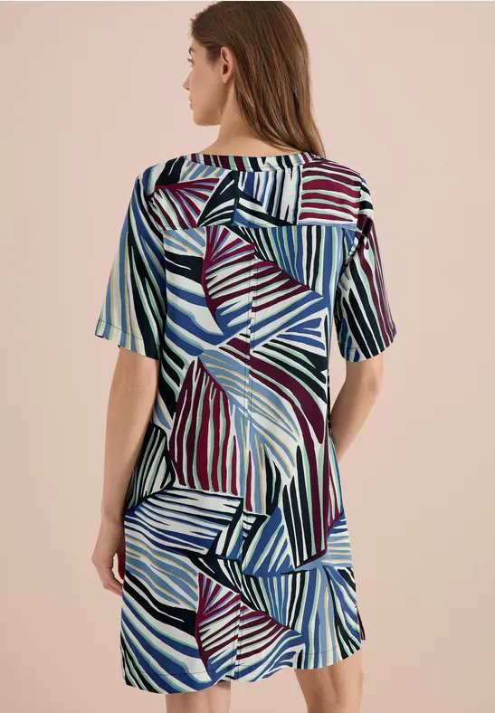 Frau von hinten in kurzärmligem Kleid mit abstraktem Streifenmuster in Blau, Lila und Weiß.