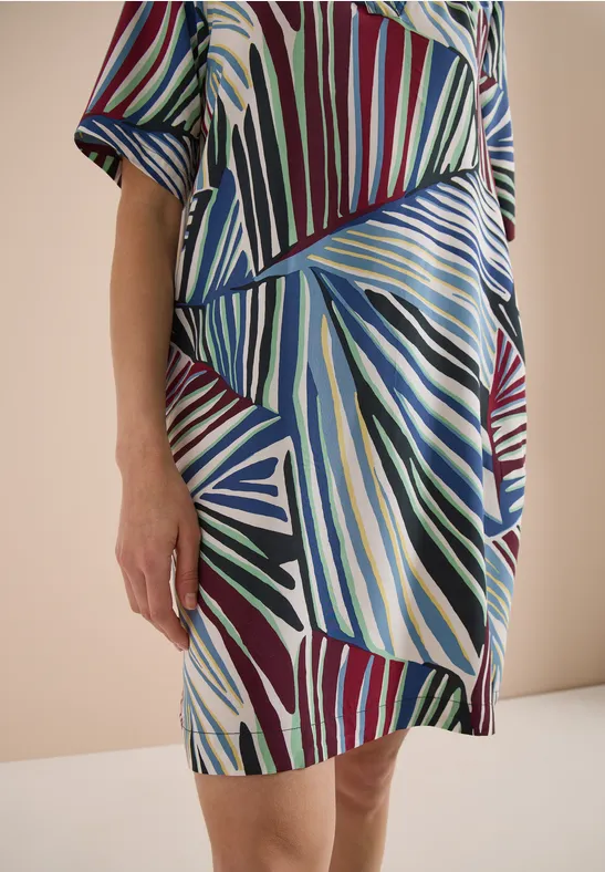 Teilansicht einer Person in einem bunten Kleid mit abstraktem geometrischem Muster.