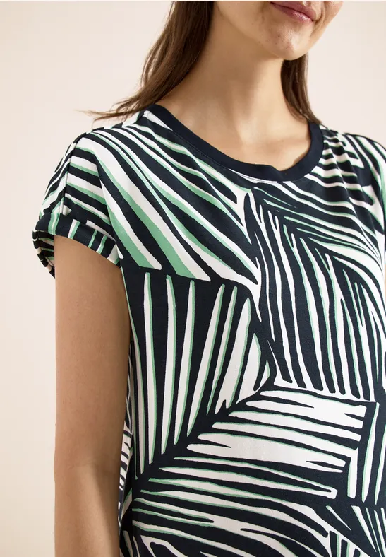 Torso féminin portant un t-shirt géométrique à rayures noires, blanches et vertes.