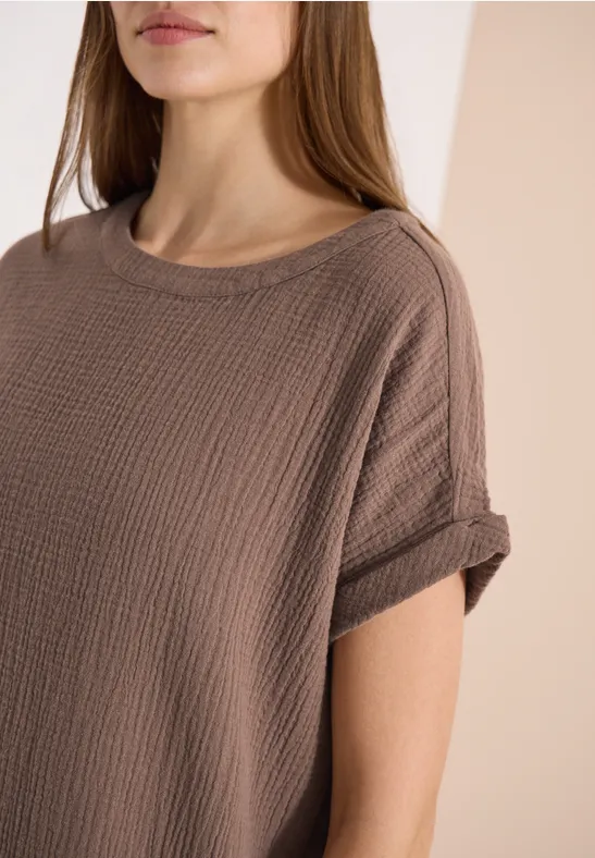 Frau im Porträt trägt ein braunes, gewaffeltes Shirt mit umgeschlagenen Ärmeln.