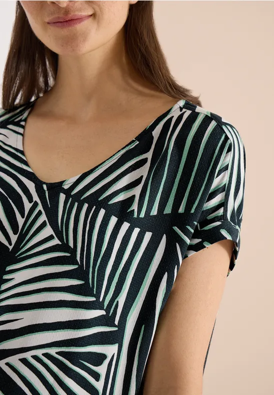 Femme en haut à motif abstrait rayé noir, blanc et vert.