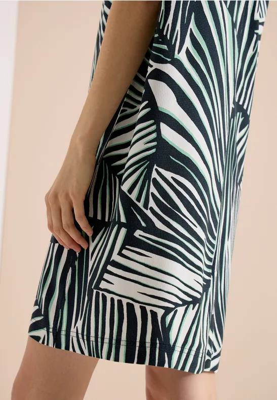 Une femme est de profil, portant une robe courte à imprimé zèbre vert et blanc.