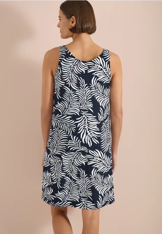 Rückansicht einer Frau in ärmellosem Kleid mit blauem Grund und weißem Blattmuster.