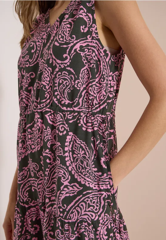 Eine Frau trägt ein ärmelloses Kleid mit pinkem Paisley-Muster auf dunklem Stoff.