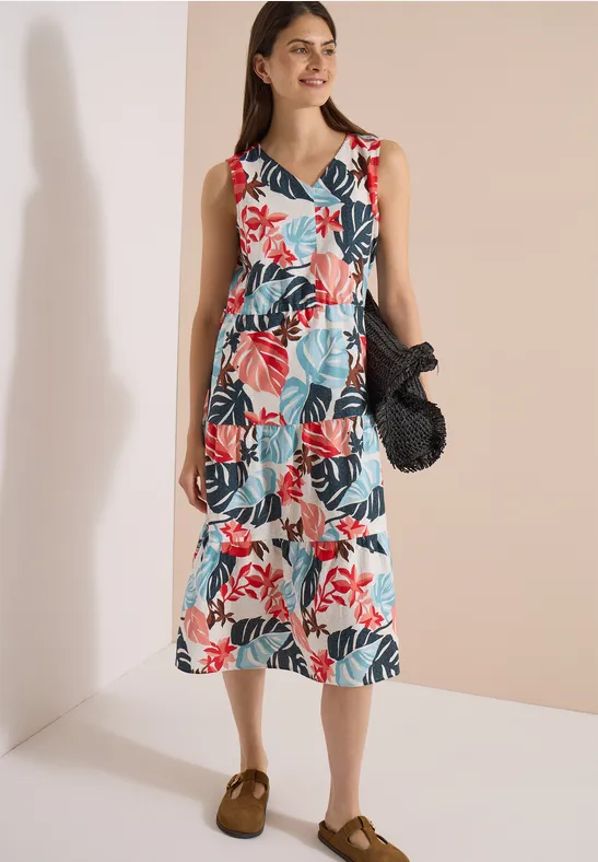 Modisches ärmelloses Midi-Kleid mit buntem tropischen Blumen- und Blattmuster, dazu braune Loafers und schwarze Tasche.