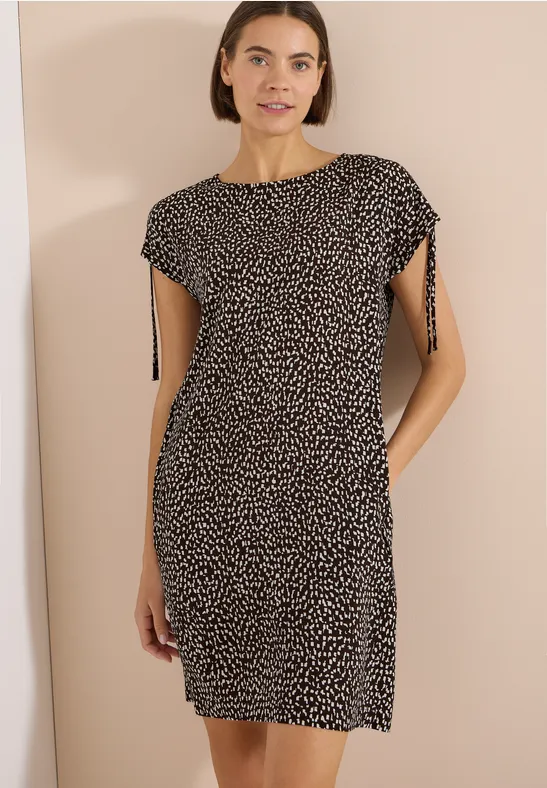 Eine Frau trägt ein knie-langes schwarzes Kleid mit kleinen weißen Punkten und Ärmeln.