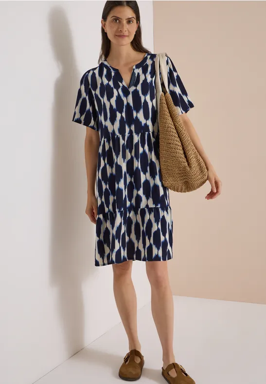 Femme en robe mi-longue bleu-blanc à motifs, manches courtes, portant un sac en paille.