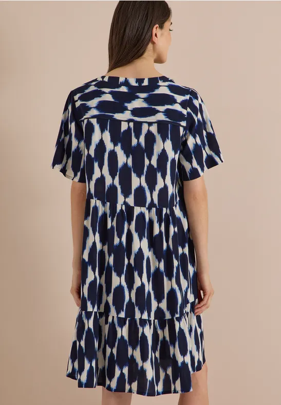 Femme de dos portant une robe courte à manches courtes, motif bleu et blanc avec volant.