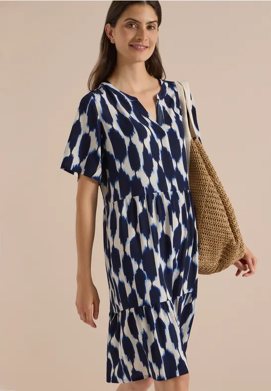 Femme en robe d’été bleu et blanc à col en V, manches courtes, avec un sac en paille