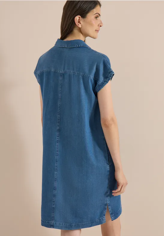 Femme vue de dos portant une robe chemise en jean à manches courtes sur fond neutre.