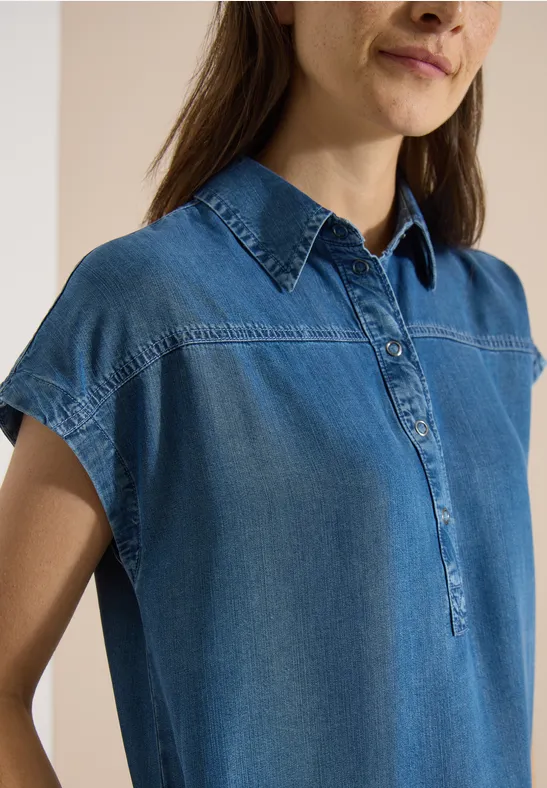 Femme portant une chemise en jean sans manches, col fermé et patte de boutonnage.