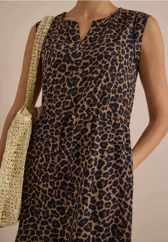 Dame in ärmellosem, blau-braunem Leopardenkleid mit V-Ausschnitt und Strohtasche.