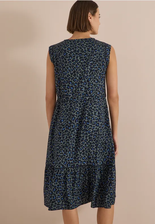 Rückenansicht: Frau in ärmellosem, knieumspielendem Kleid mit blau-schwarzem Animal-Print vor schlichtem Hintergrund.