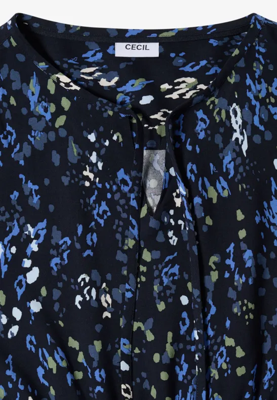 Schwarze Bluse mit abstraktem blau-grün-weißem Fleckenmuster und kleinem vorgesetztem Knoten am Rundhalsausschnitt.