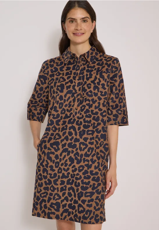 Une femme porte une robe mi-longue à manches 3/4, imprimé léopard marron et noir, avec poches latérales.