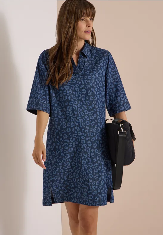 Femme en robe-chemise midi bleu foncé à motifs discrets, manches mi-longues, tenant un sac noir.