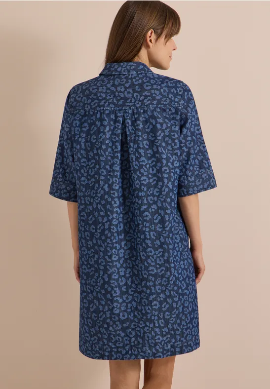 Femme vue de dos portant une robe-chemise bleue ample à manches courtes et motif discret.