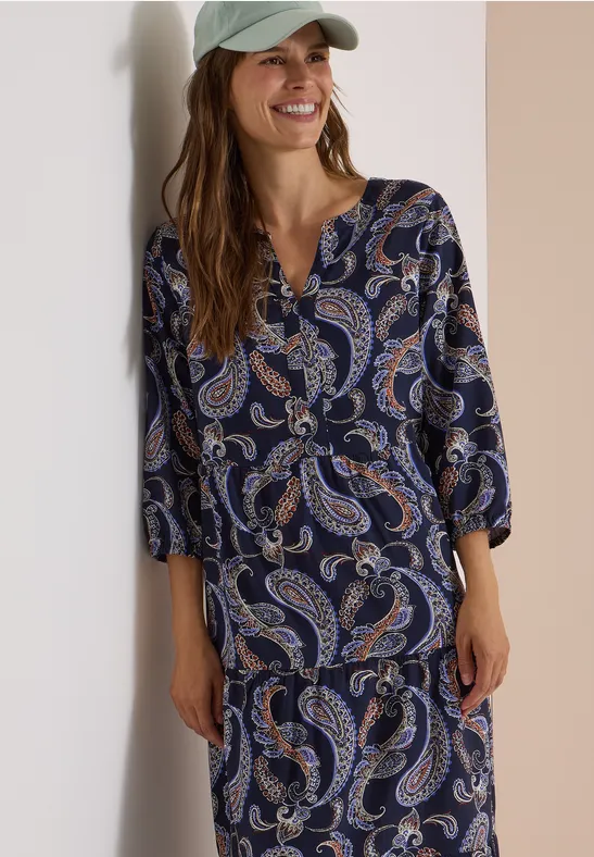 Femme portant un haut à motif cachemire bleu et une jupe assortie, souriante.