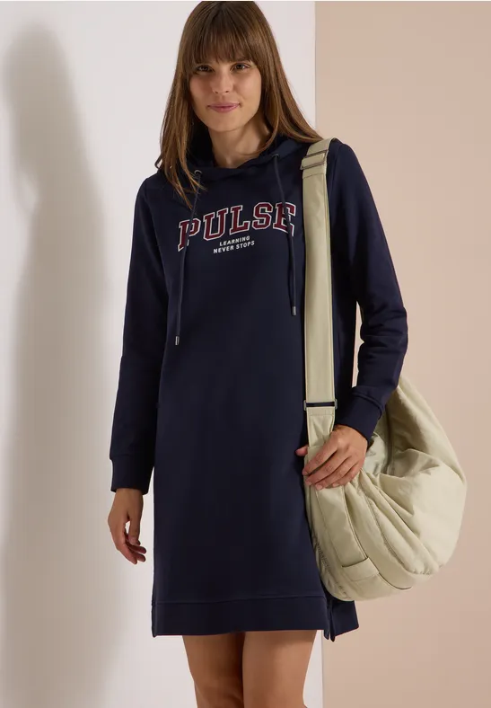 Femme en robe à capuche bleu marine « PULSAR », porte un grand sac bandoulière matelassé beige.