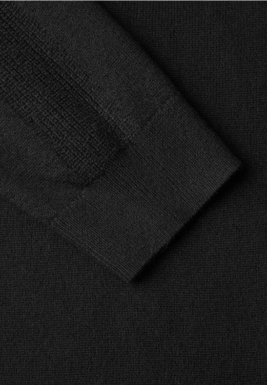 Gros plan sur un pull en maille noire, détail du poignet et texture fine du tissu.
