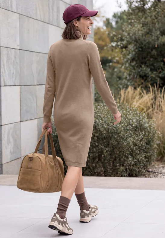 Femme vue de dos, robe midi beige, baskets et casquette marron, portant un grand sac.