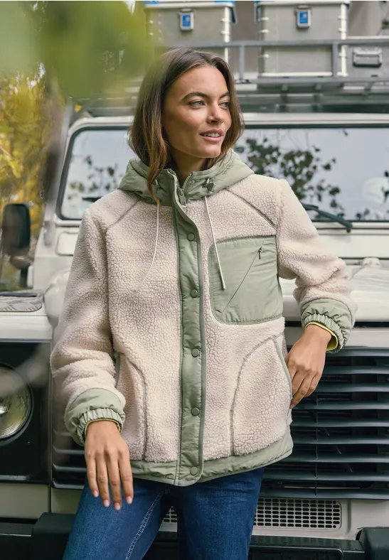 Person trägt helle Fleecejacke mit grünen Akzenten, steht vor einem weißen Geländewagen.