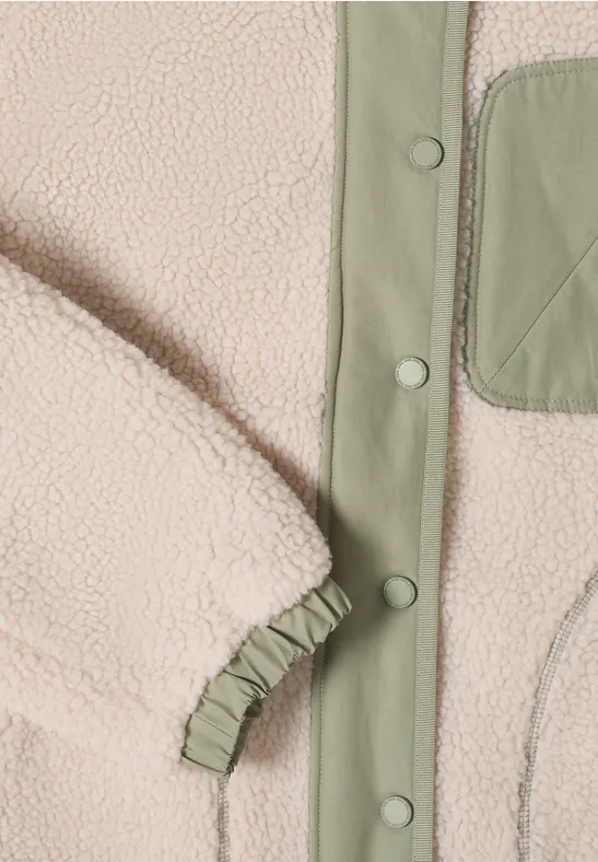 Nahaufnahme einer cremefarbenen Teddyjacke mit grüner Paspel, Druckknöpfen und gerafftem Ärmelbündchen.