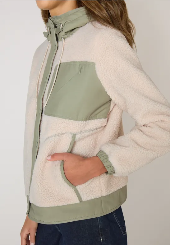 Beige Teddy-Fleecejacke mit olivgrünen Einsätzen und Reißverschluss, getragen zu Jeans.