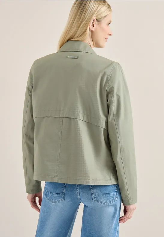 Frau in khakigrüner Jacke und blauer Jeans, Rückansicht