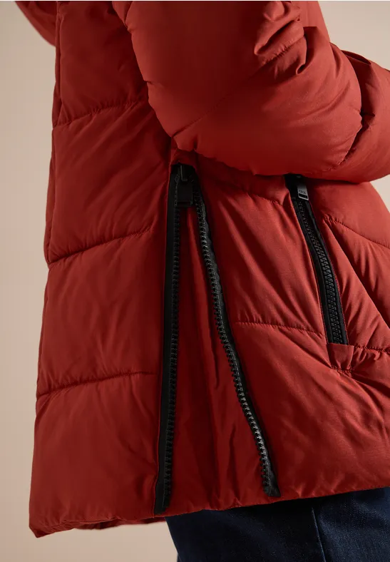 Roter Steppmantel mit schwarzem Reißverschluss und seitlichen Zipper-Details, getragen zu blauer Hose.