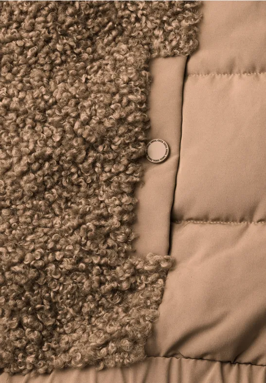 Nahaufnahme einer Jacke mit links flauschigem Lammfell, rechts gestepptem Stoff und mittigem Metallknopf.