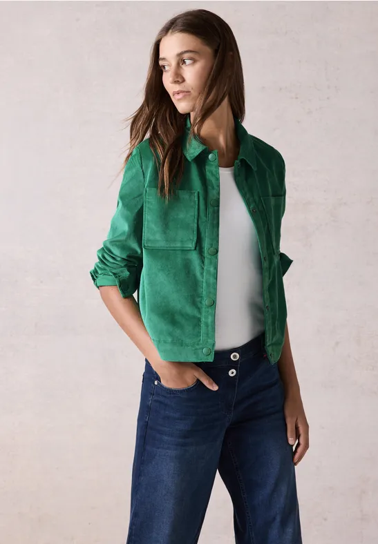 Frau mit grüner Jacke, weißem Shirt und Jeans blickt zur Seite.
