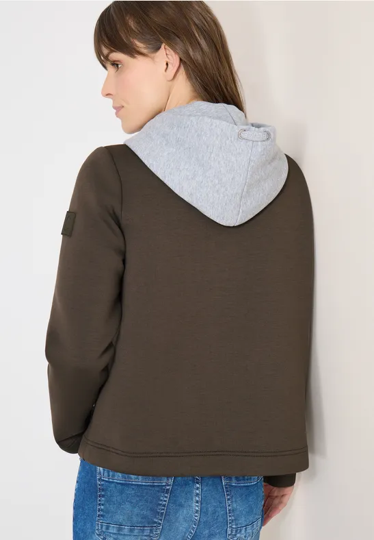 Rückansicht einer Person in dunkelbrauner Jacke mit grauer Kapuze und blauen Jeans