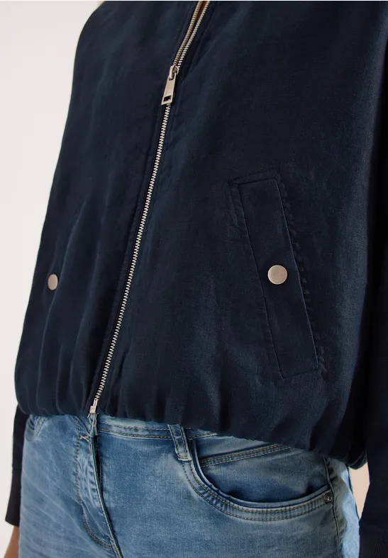 Dunkelblaue Jacke mit Reißverschluss und blaue Jeans, nur Oberkörper sichtbar.