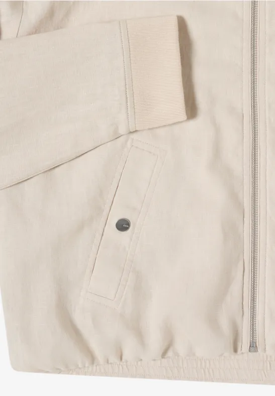 Nahaufnahme einer hellbeigen Jacke mit Reißverschluss, aufgesetzter Tasche mit Druckknopf und elastischem Saum.
