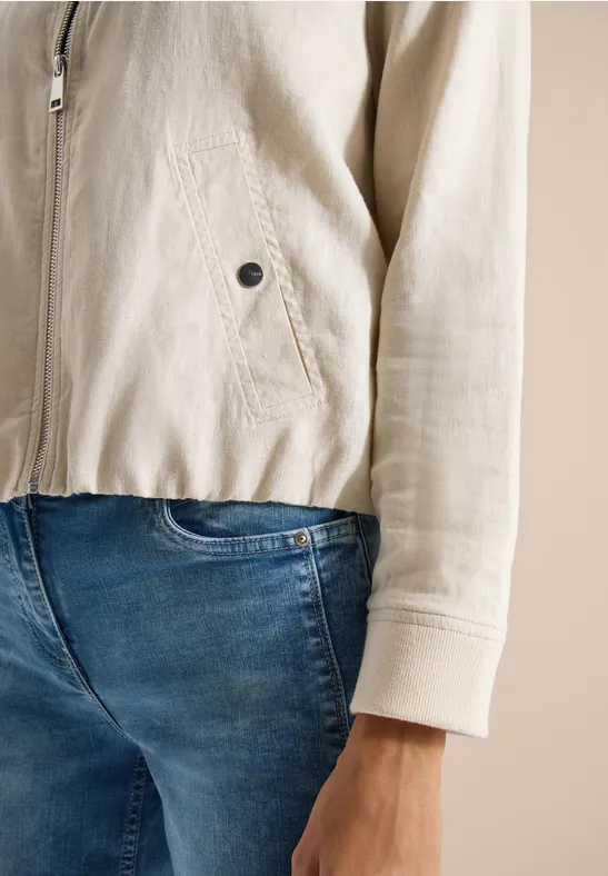 Nahaufnahme einer Person in hellbeiger Jacke und blauen Jeans, Fokus auf Rumpf und Hand.