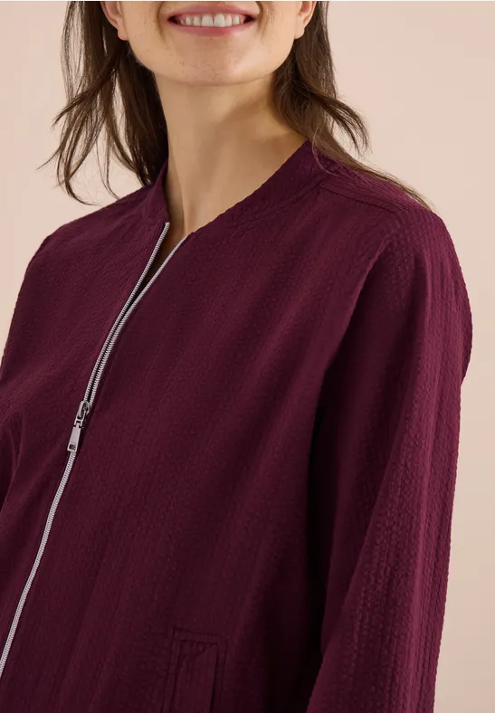 Frau in leichter, weinroter Jacke mit feiner Struktur und silbernem Reißverschluss