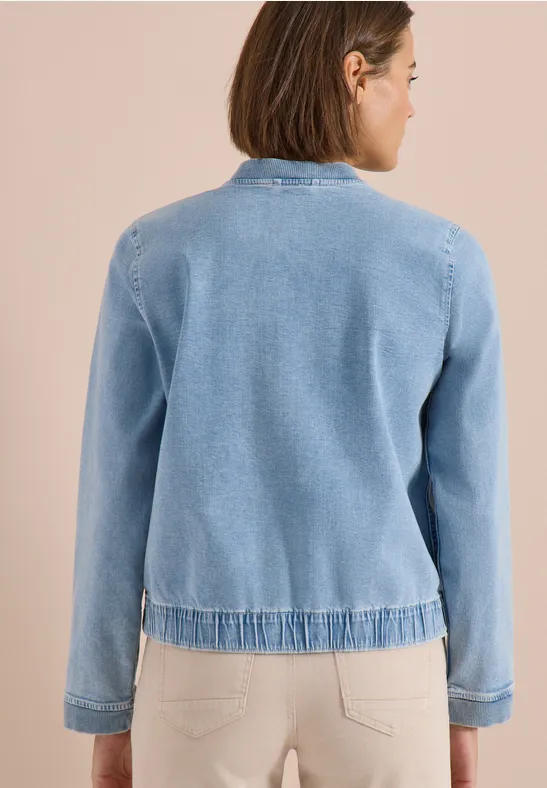 Frau mit hellblauer Strickjacke steht mit dem Rücken zur Kamera.