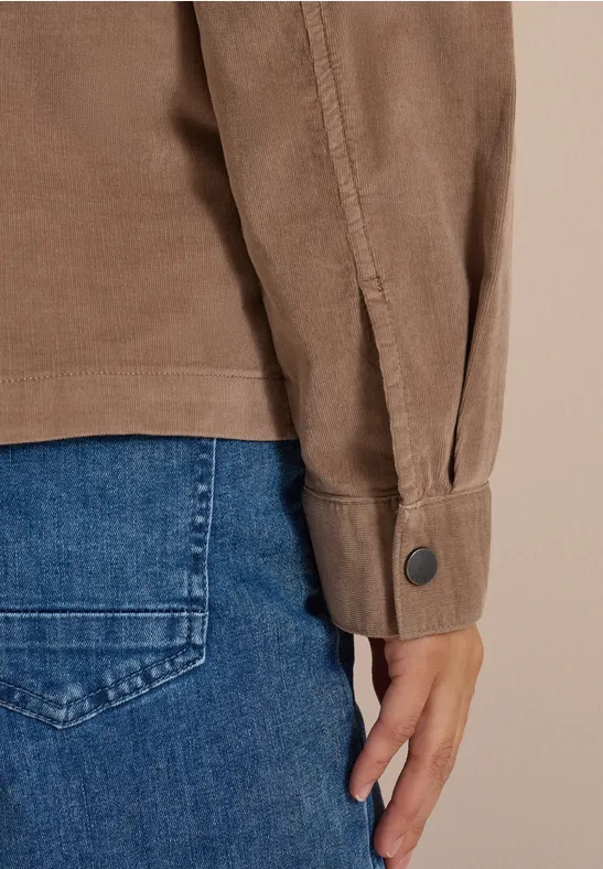 Nahaufnahme eines Arms in braunem Hemd und Hand neben der Hosentasche einer blauen Jeans.