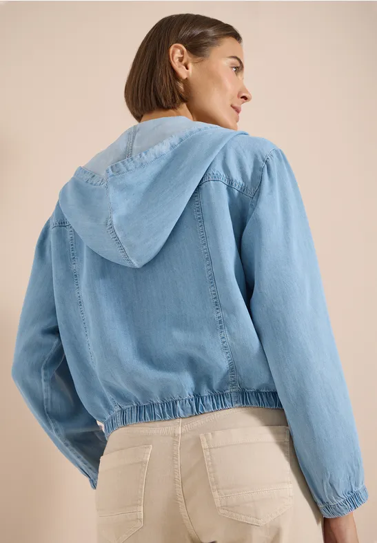 Rückansicht einer Frau in hellblauer Jeansjacke mit Kapuze.