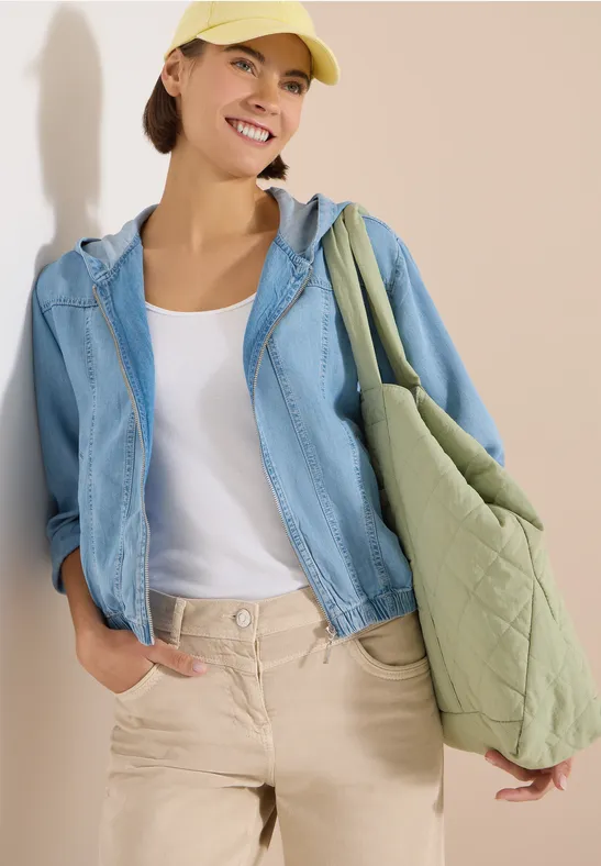 Person trägt weißes Top, hellblaue Jeansjacke, beige Hose und gesteppte grüne Tasche.
