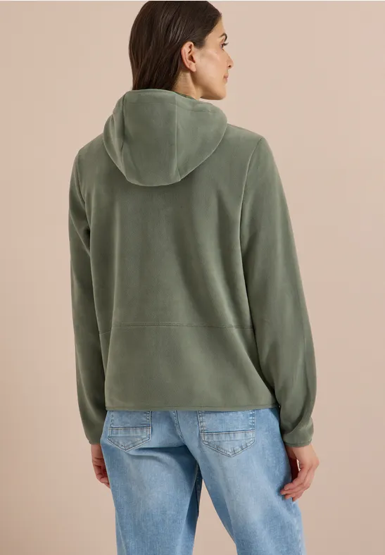 Frau von hinten in grüner Kapuzenjacke und Jeans, blickt leicht zur Seite