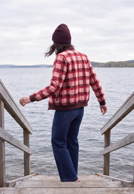 Personne en veste à carreaux rouge et bonnet sur un ponton, regardant un lac paisible.