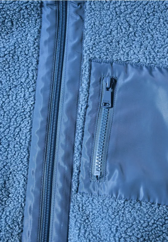 Nahaufnahme einer blauen Fleecejacke mit Hauptreißverschluss und aufgesetzter Reißverschlusstasche.