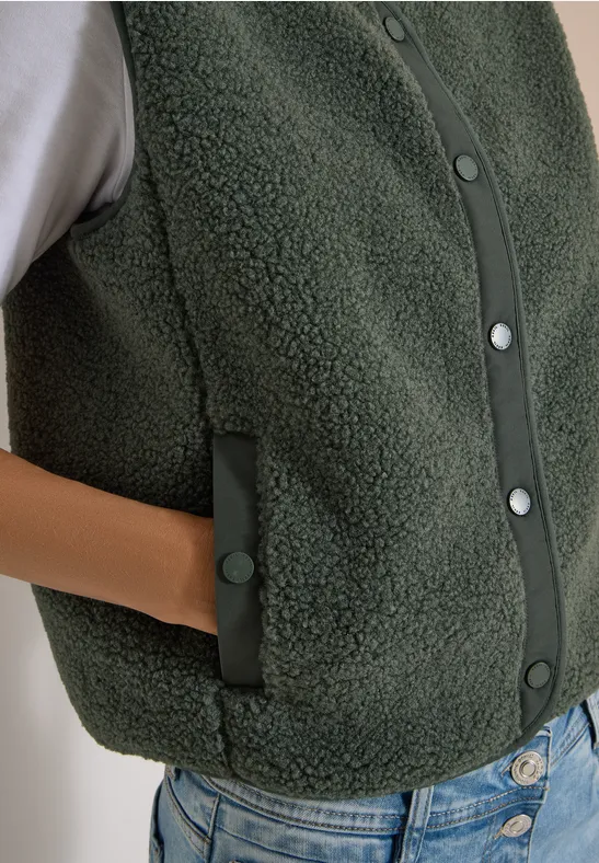 Veste en polaire teddy vert foncé à pressions avec poches latérales, portée sur un t-shirt blanc et jean.