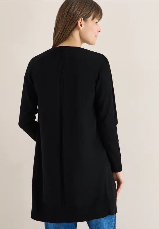 Frau steht mit dem Rücken zur Kamera und trägt einen langen schwarzen Cardigan.