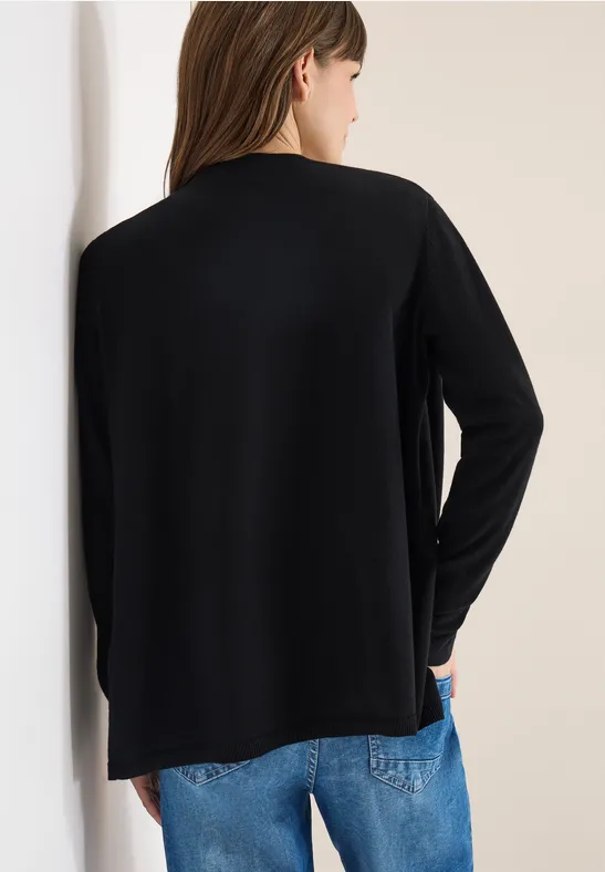 Rückansicht einer Person in schwarzem Langarmshirt und blauen Jeans vor heller Wand.