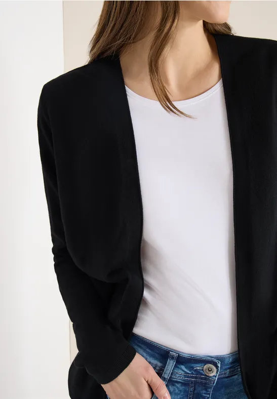 Eine Frau im weißen Shirt und schwarzer Strickjacke, nur der Oberkörper ist zu sehen.