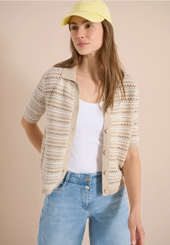 Femme portant un gilet crochet beige sur débardeur blanc, jean et casquette jaune.